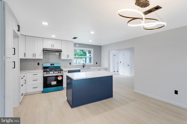 kitchen with stainless steel gas range, sink, decorative light fixtures, a center island, and white cabinets