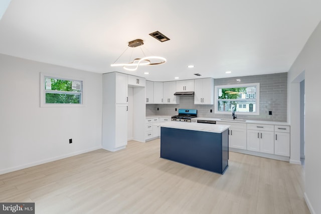 kitchen with sink, stainless steel stove, white cabinetry, hanging light fixtures, and a center island