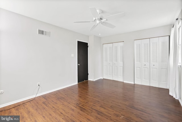 unfurnished bedroom featuring ceiling fan, dark hardwood / wood-style floors, and two closets