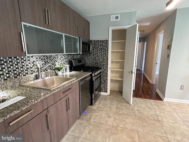 kitchen featuring sink, light tile patterned floors, stainless steel appliances, and dark stone counters