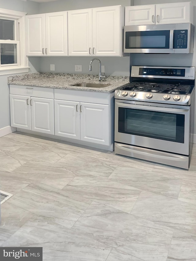 kitchen featuring white cabinetry, sink, stainless steel appliances, and light stone countertops