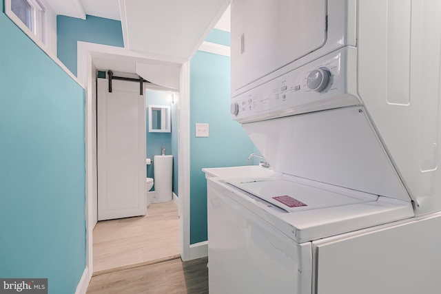 laundry room featuring stacked washer / dryer, a barn door, light hardwood / wood-style floors, and sink