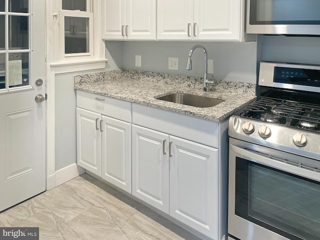 kitchen with white cabinetry, sink, light stone countertops, and appliances with stainless steel finishes