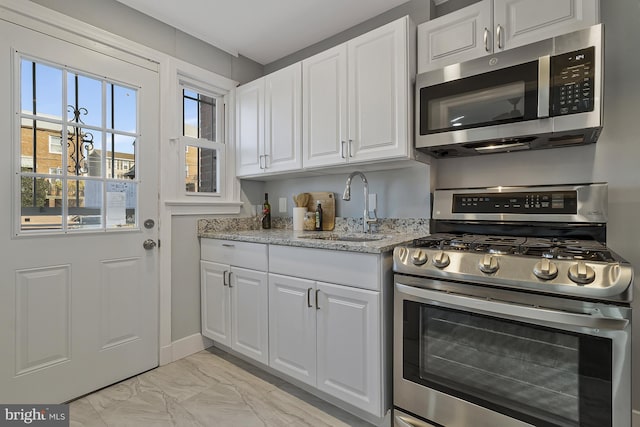 kitchen featuring stainless steel appliances, white cabinetry, light stone countertops, and sink