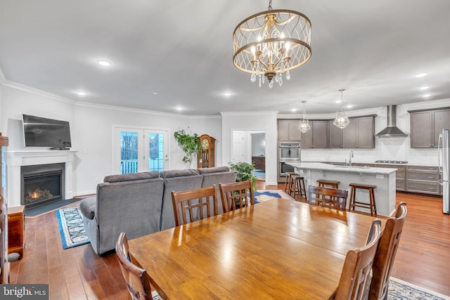 dining area featuring sink, wood-type flooring, ornamental molding, and a chandelier