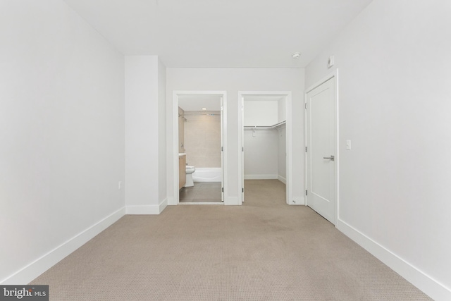 unfurnished bedroom with a closet, connected bathroom, a spacious closet, and light carpet