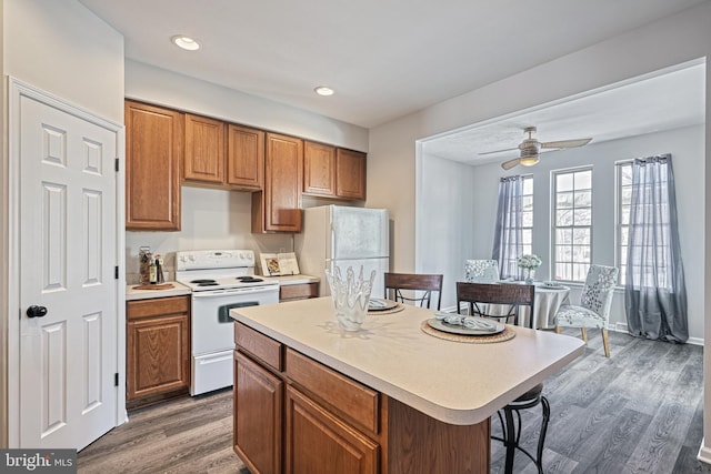 kitchen with a breakfast bar, a center island, ceiling fan, dark wood-type flooring, and white appliances