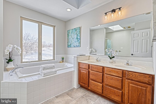 bathroom featuring tile patterned floors, vanity, tiled bath, and a skylight