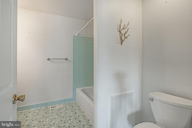 bathroom featuring tile patterned flooring, tiled shower / bath combo, and toilet