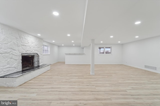 basement featuring a stone fireplace and light hardwood / wood-style flooring