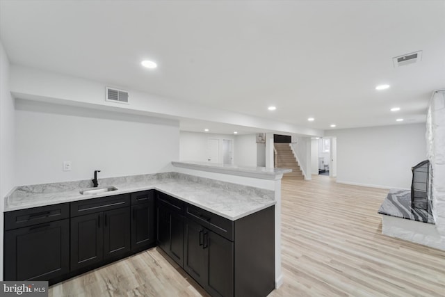 kitchen featuring sink, light hardwood / wood-style flooring, light stone countertops, and kitchen peninsula