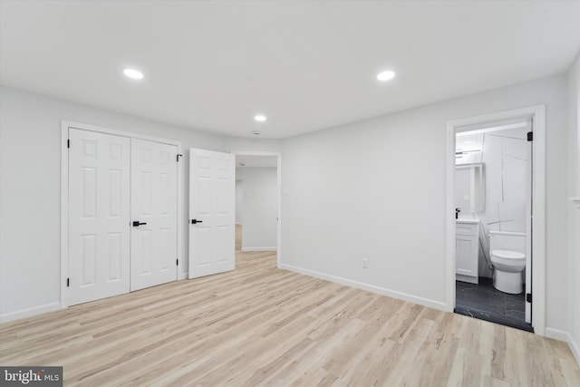 unfurnished bedroom with ensuite bath, light hardwood / wood-style floors, and a closet