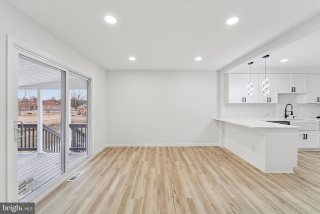 kitchen featuring white cabinetry, light hardwood / wood-style flooring, kitchen peninsula, pendant lighting, and decorative backsplash