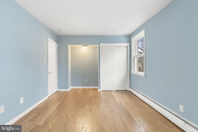 unfurnished bedroom featuring light wood-type flooring, baseboard heating, and a closet