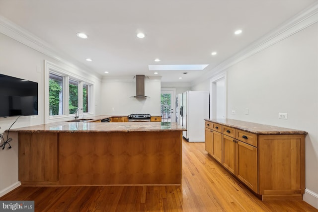 kitchen featuring wall chimney exhaust hood, sink, a skylight, kitchen peninsula, and white fridge