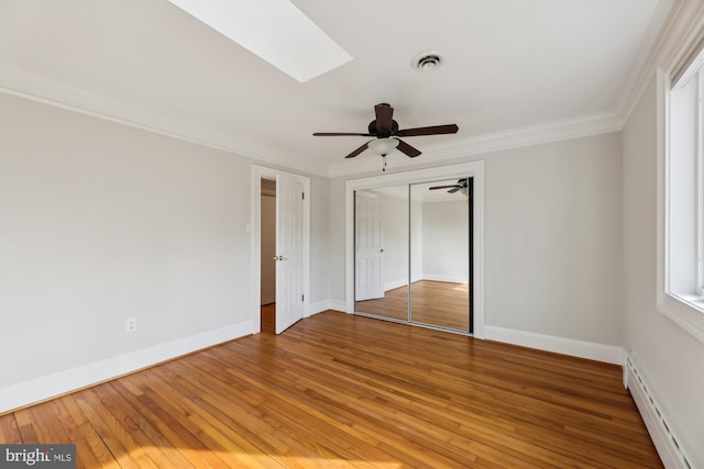 unfurnished bedroom with hardwood / wood-style flooring, ceiling fan, a skylight, ornamental molding, and a baseboard radiator