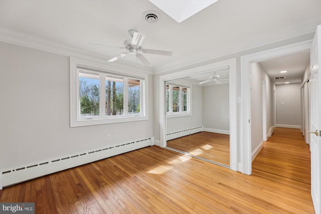 unfurnished room with crown molding, a baseboard radiator, a skylight, and light wood-type flooring