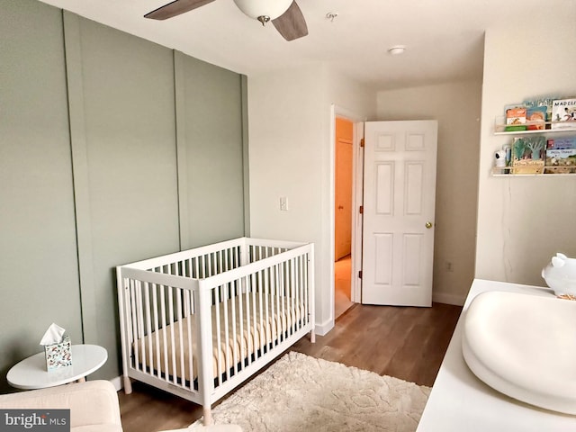 bedroom with a nursery area, ceiling fan, dark hardwood / wood-style floors, and a closet