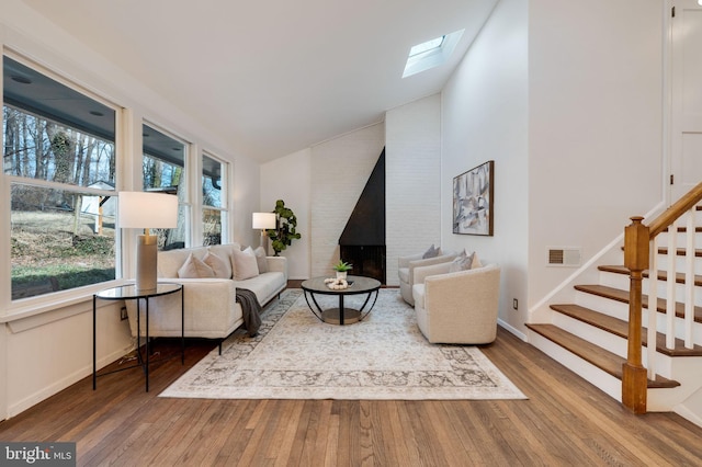 living room featuring baseboards, visible vents, lofted ceiling with skylight, stairway, and wood finished floors