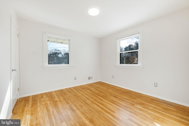 empty room featuring baseboards, visible vents, and hardwood / wood-style floors