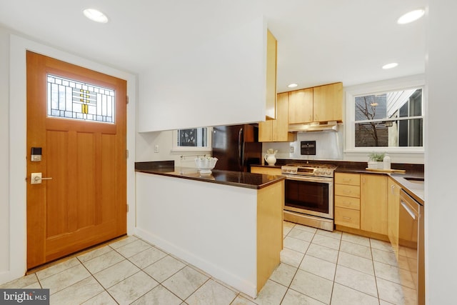 kitchen featuring light tile patterned floors, dark countertops, appliances with stainless steel finishes, a peninsula, and under cabinet range hood