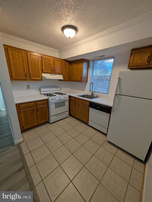 kitchen featuring brown cabinetry, white appliances, a sink, and under cabinet range hood