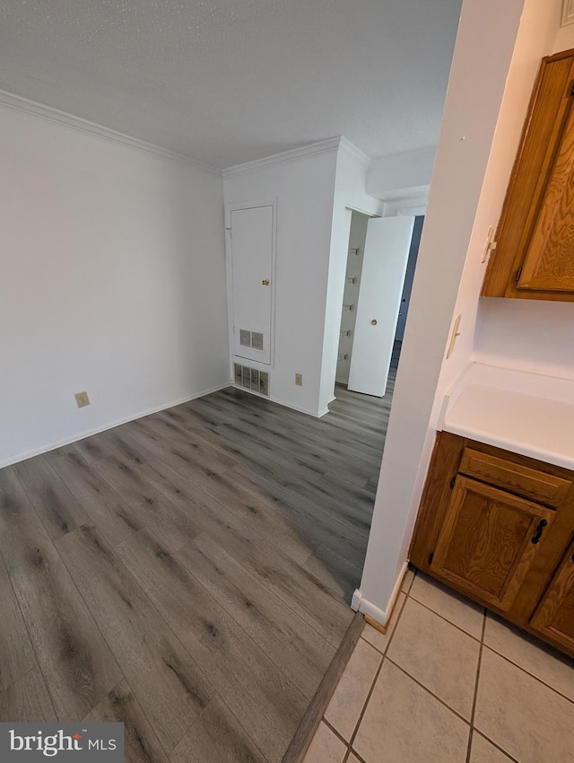 interior space with baseboards, light wood-style flooring, visible vents, and crown molding