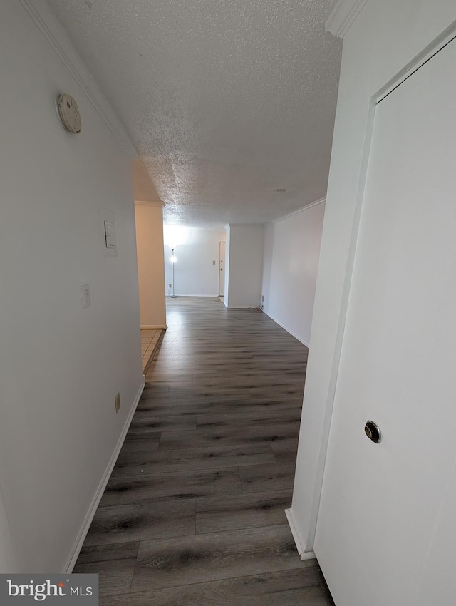 corridor featuring a textured ceiling, baseboards, wood finished floors, and crown molding