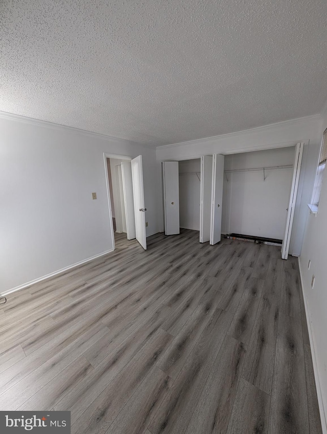 unfurnished bedroom with a textured ceiling, multiple closets, and wood finished floors