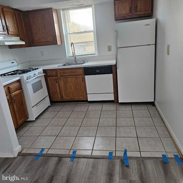 kitchen with light tile patterned floors, under cabinet range hood, white appliances, a sink, and light countertops