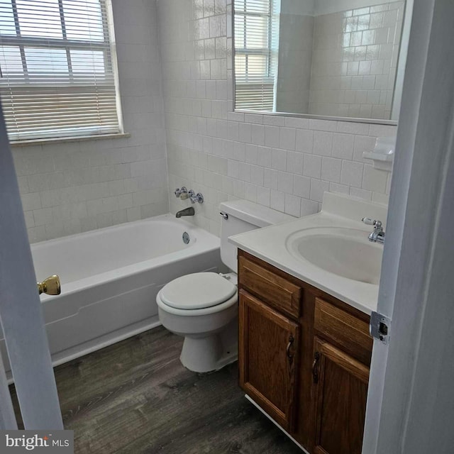 bathroom with toilet, wood finished floors, vanity, tile walls, and a bath