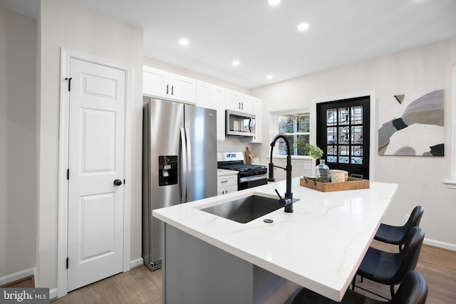 kitchen with sink, a breakfast bar area, white cabinetry, stainless steel appliances, and a kitchen island with sink