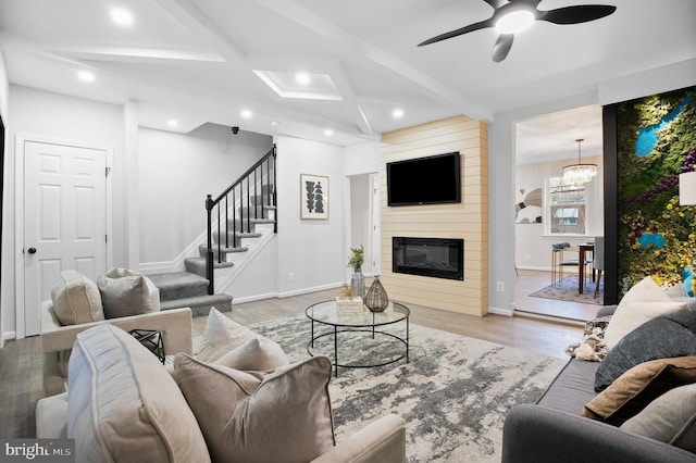 living room with light hardwood / wood-style flooring, beam ceiling, coffered ceiling, a large fireplace, and ceiling fan with notable chandelier