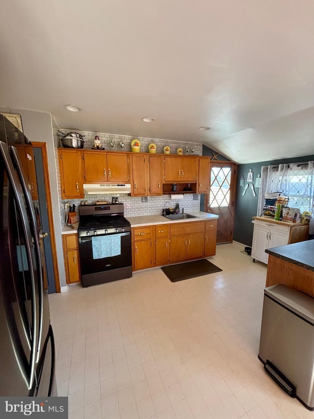 kitchen with lofted ceiling, sink, black fridge, stainless steel range with gas cooktop, and decorative backsplash