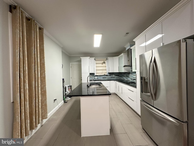 kitchen with sink, a center island with sink, stainless steel fridge, decorative backsplash, and white cabinets