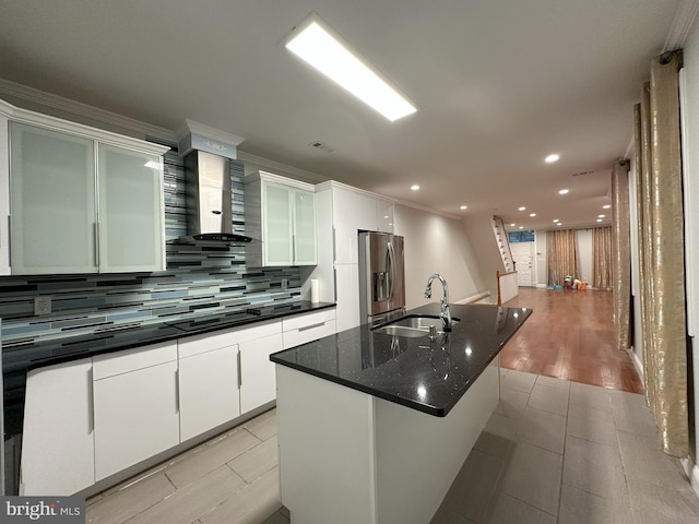 kitchen featuring sink, white cabinets, a kitchen island with sink, stainless steel refrigerator with ice dispenser, and wall chimney exhaust hood