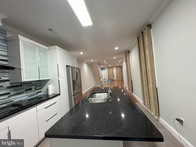 kitchen featuring stainless steel refrigerator with ice dispenser, sink, white cabinets, a large island, and backsplash