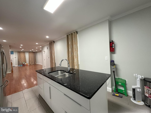 kitchen with sink, dark stone countertops, ornamental molding, an island with sink, and white cabinets