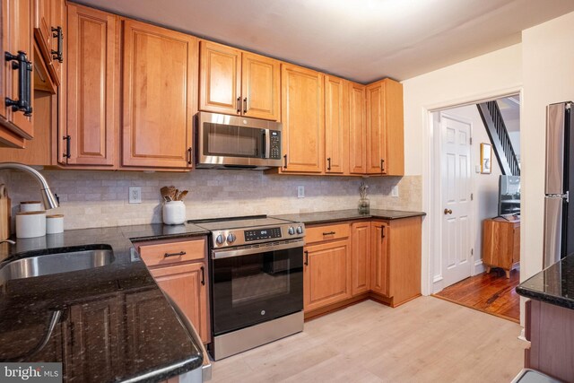 kitchen with sink, tasteful backsplash, appliances with stainless steel finishes, dark stone counters, and light hardwood / wood-style floors