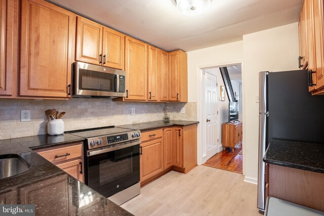 kitchen featuring tasteful backsplash, appliances with stainless steel finishes, light hardwood / wood-style floors, and dark stone countertops