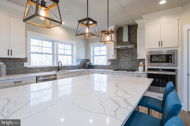 kitchen with light stone counters, appliances with stainless steel finishes, wall chimney exhaust hood, and hanging light fixtures