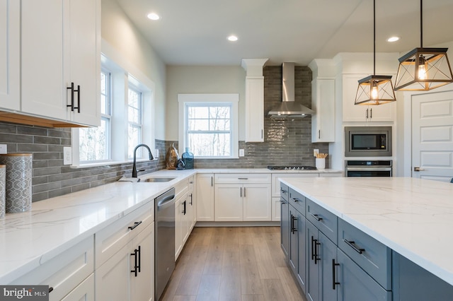 kitchen featuring sink, decorative light fixtures, appliances with stainless steel finishes, wall chimney range hood, and white cabinets