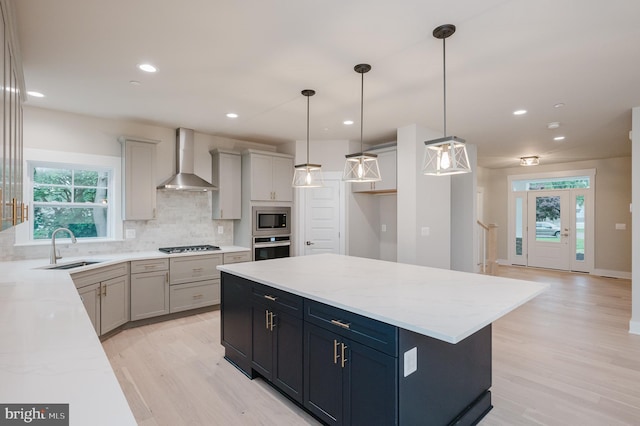 kitchen featuring wall chimney range hood, decorative light fixtures, stainless steel appliances, and a kitchen island