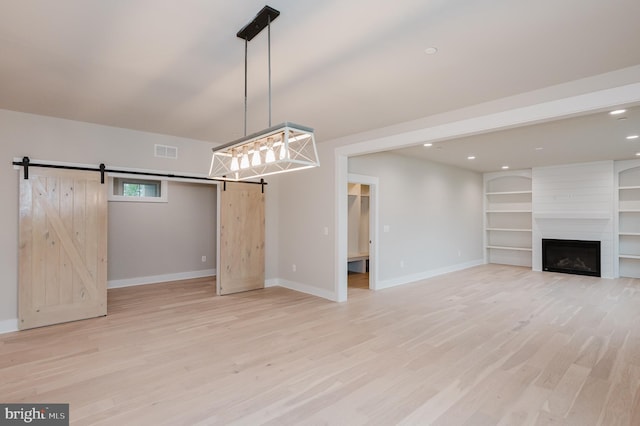 unfurnished living room featuring a large fireplace, light hardwood / wood-style flooring, a barn door, and built in shelves