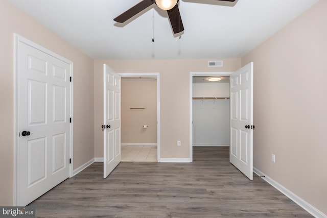 unfurnished bedroom featuring hardwood / wood-style flooring, ceiling fan, a spacious closet, and a closet