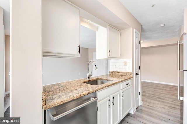 kitchen with tasteful backsplash, dishwasher, sink, white cabinets, and light stone countertops