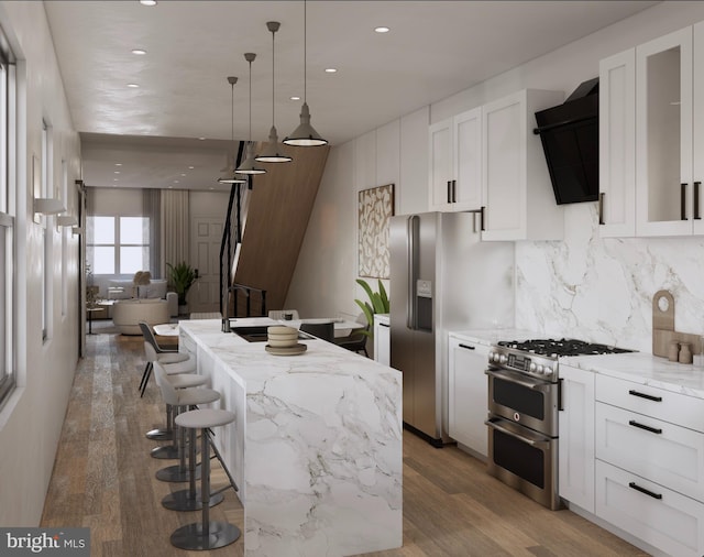 kitchen with white cabinetry, hanging light fixtures, appliances with stainless steel finishes, a kitchen island, and exhaust hood