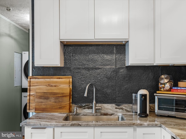 kitchen featuring white cabinetry, stacked washer and dryer, ornamental molding, and sink