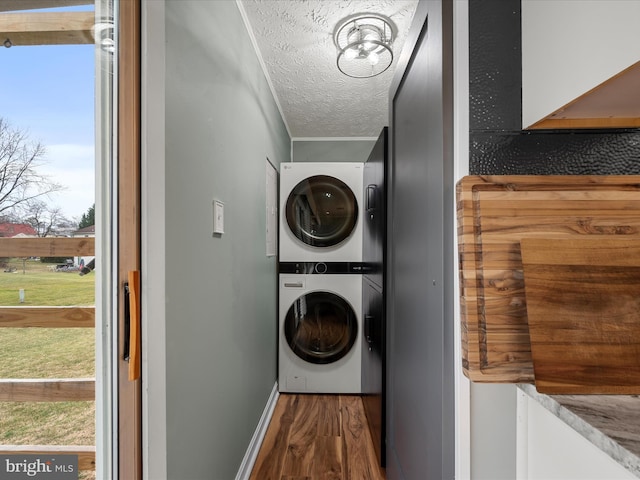 washroom featuring wood-type flooring, stacked washing maching and dryer, a textured ceiling, and plenty of natural light