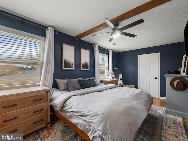 bedroom featuring ceiling fan, beam ceiling, a textured ceiling, and hardwood / wood-style flooring